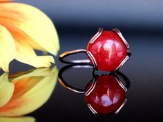 a red ring sitting on top of a black surface next to a yellow and orange flower