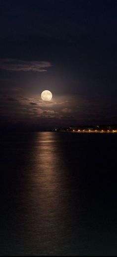 the full moon shines brightly in the night sky over the ocean and shore line