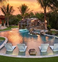 an outdoor swimming pool surrounded by palm trees and lawn chairs with lights on the side