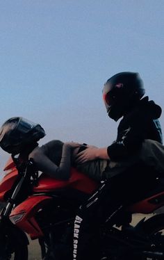 a man riding on the back of a red motorcycle next to another person wearing a helmet