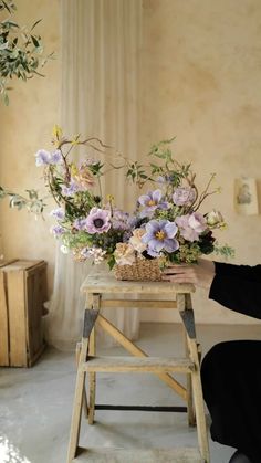 a woman sitting on a stool holding a basket filled with flowers