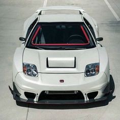 the front end of a white sports car parked in a parking lot with its hood up