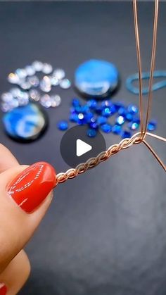 a person holding a piece of metal wire with blue and red beads in the background