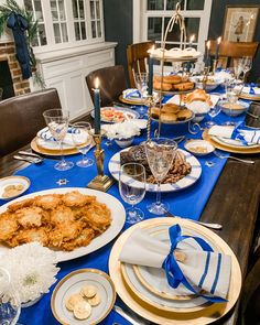 a dining room table is set with blue and gold plates, silverware, and candles