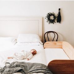 a baby laying on top of a white bed next to a wooden dresser and chair