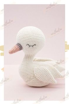 a crocheted white duck sitting on top of a pink surface with its eyes closed