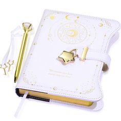 an open notebook with a gold pen and star charm on it, sitting next to the book