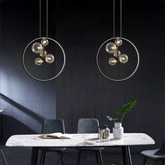 two circular lights hanging from the ceiling above a table with chairs and a vase on it