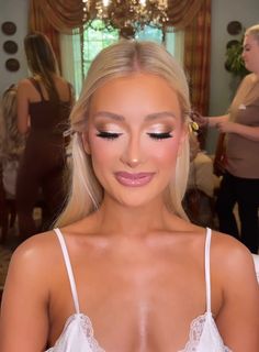 a woman with long blonde hair wearing a white dress and makeup looks at the camera