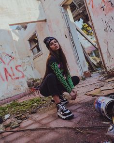 a young woman squatting on the ground in front of an abandoned building with graffiti