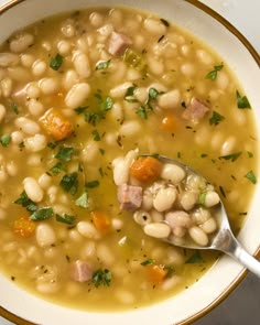 a white bowl filled with beans and ham on top of a table next to a spoon