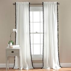 white curtains with black trim hanging on a window sill in front of a wooden floor