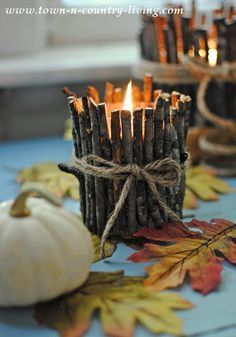 some candles are sitting on a table with autumn leaves and pumpkins around them,