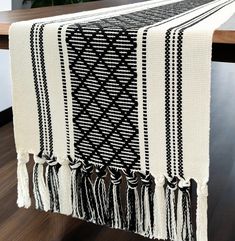 a black and white table runner with tassels on the edge, sitting on a wooden table