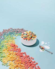 cereal in a bowl and spoon on a blue background with rainbow colored cereal scattered around it