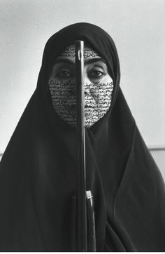 a woman wearing a black veil and holding a microphone in front of her face with words written on it