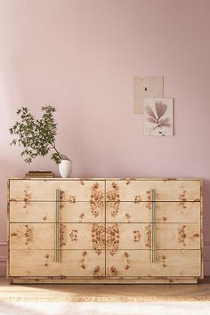 a large wooden dresser sitting next to a plant in a living room with pink walls