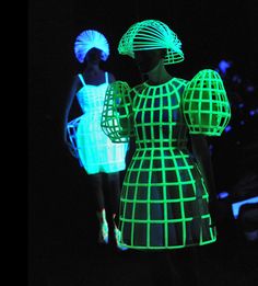 two women in neon dresses and hats walking down the runway at night with their hands on their hips