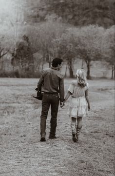 a man and woman walking through a field holding hands