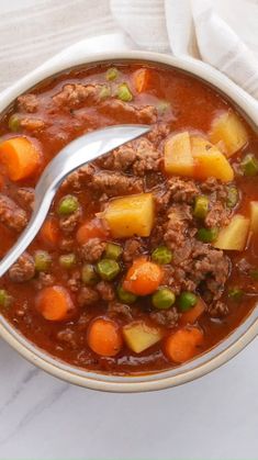 a bowl of beef stew with carrots, peas and potatoes on a marble table