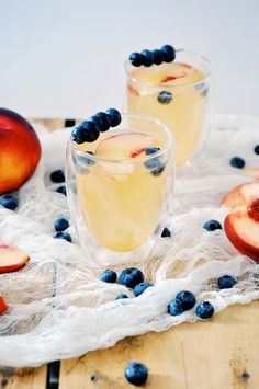 two glasses filled with blueberries and peaches on top of a white table cloth