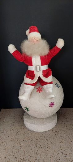 a santa clause figurine sitting on top of a snow globe with his arms in the air