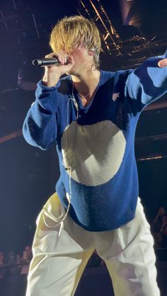 a male in a blue and white sweater is on stage with his hands out to the side