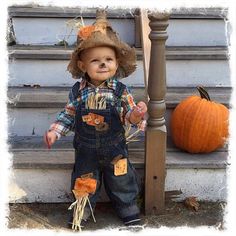 a little boy wearing overalls and a cowboy hat standing next to a stair case