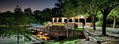 a wooden bridge over a small pond at night with lights on the walkway and trees surrounding it