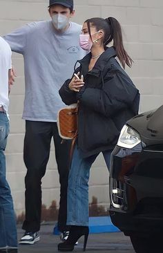 a woman wearing a face mask while standing next to a man in a black jacket