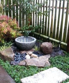 a small garden with rocks, grass and water feature in the center is surrounded by bamboo fencing