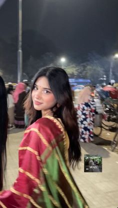 a woman in a red and green sari is walking down the street at night