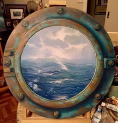 a painting is shown in an old porthole style frame on a table next to other items