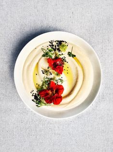 a white plate topped with hummus and red flowers