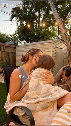 a woman holding a baby wrapped in a blanket while sitting next to another woman on a chair