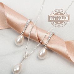 two necklaces with pearls on them sitting next to a pink ribbon