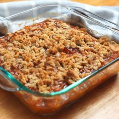 a glass casserole dish filled with food on top of a wooden table next to a napkin