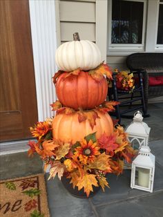 three pumpkins stacked on top of each other in front of a house with fall leaves