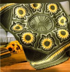 a crocheted blanket with sunflowers in the center on a wooden table