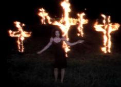 a woman standing in front of a cross made out of fire with her arms outstretched