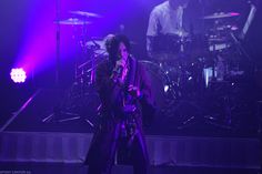 a man standing in front of a microphone on top of a stage with purple lights