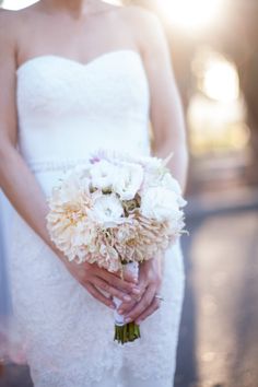 a woman in a white dress holding a bouquet of flowers on her wedding day with the sun shining behind her