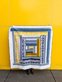 a blue and yellow quilt sitting on top of a floor next to a yellow wall