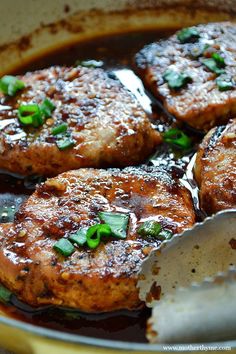 some meat is cooking in a skillet with sauce and green onions on the side