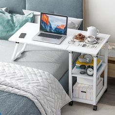 a laptop computer sitting on top of a white desk next to a bed with pillows