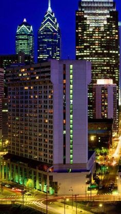 the city skyline is lit up at night with skyscrapers in the foreground and cars on the road