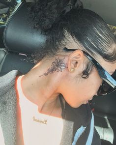 a woman with a flower tattoo on her neck and behind her ear, sitting in the back seat of a car