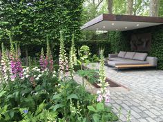 an outdoor living area with couches and flowers in the foreground, surrounded by greenery