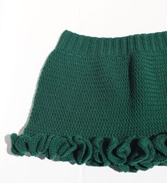 a green knitted skirt with ruffles on the front and bottom, sitting on a white surface