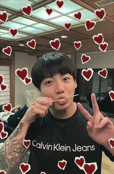 a young man holding a toothbrush up to his mouth with hearts all over him